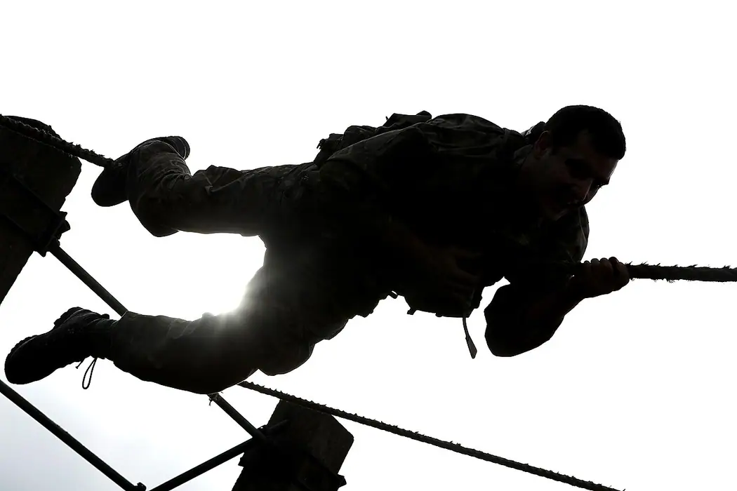 Royal Marines recruit traversing an overhead rope obstacle during commando training